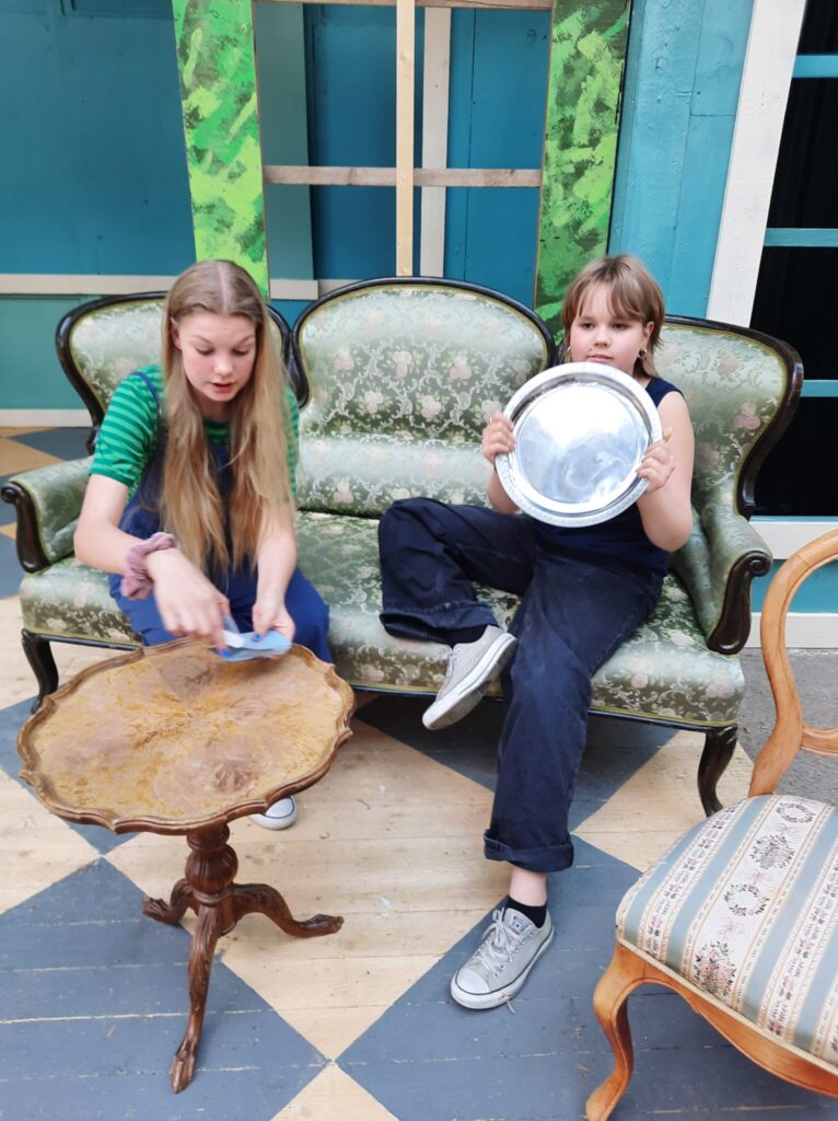 Two girls sitting on a couch, other one is holding a silver plate.