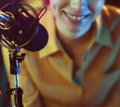 In front of the microphone, a woman smiles in the background.