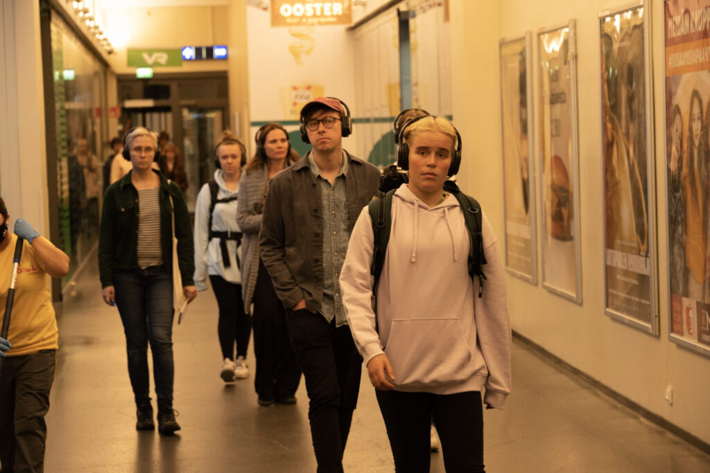 The participants of the show walk indoors with headphones on.